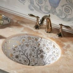 a bathroom sink with an artistic design on the bowl and gold faucet handles