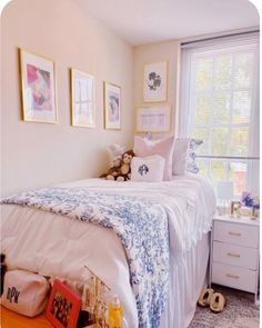 a white bed sitting next to a window with pictures on the wall above it and a teddy bear