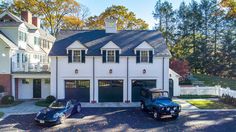 two cars are parked in front of a white house with black garage doors and windows