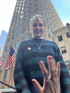 a man standing in front of a tall building holding his hand up to the camera