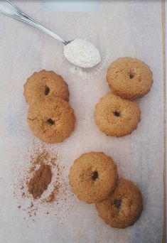 four cookies with powdered sugar on top and spoon next to them sitting on a piece of paper