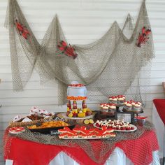 a table topped with lots of food and desserts next to a red chair in front of a white wall