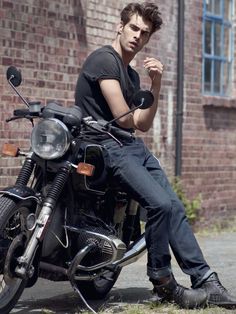 a man sitting on top of a motorcycle next to a brick building and holding his fist