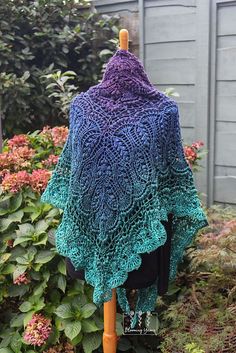 a blue and green crocheted shawl sitting on top of a wooden pole