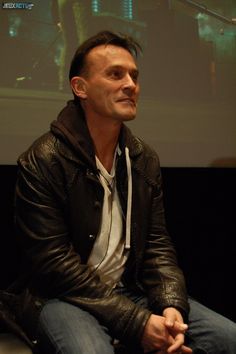 a man sitting in front of a projector screen wearing a black jacket and white shirt