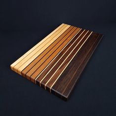 a wooden cutting board sitting on top of a black surface with vertical strips of wood