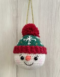 a crocheted snowman ornament hanging on a white wooden wall with a gold chain