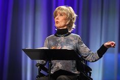 a woman sitting in a wheel chair with her hands out to the side while speaking into a microphone