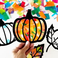 a hand holding up a cutout of a pumpkin surrounded by fall leaves and paper