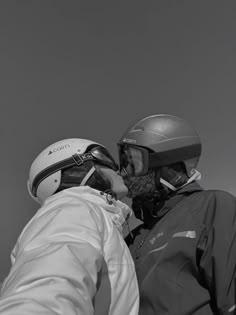 black and white photograph of two people with helmets on their heads, one kissing the other