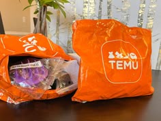 two orange bags sitting next to each other on top of a wooden table in front of a potted plant