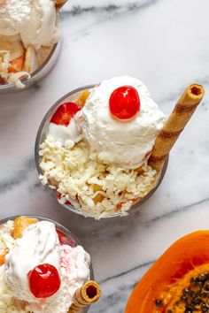 three bowls filled with ice cream and fruit on top of a marble countertop next to an orange bowl