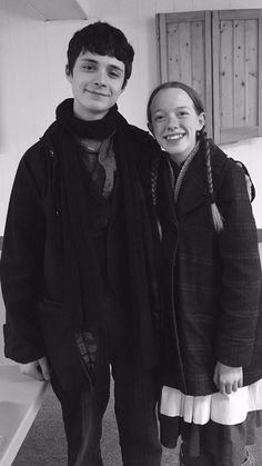 two young people standing next to each other in a room with white walls and wooden cabinets