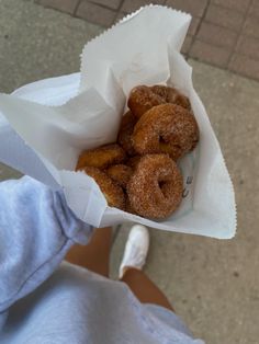 a person holding a paper bag filled with doughnuts on top of a sidewalk