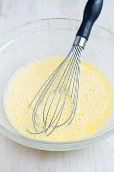 a glass bowl filled with yellow liquid and whisk