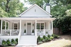 a small white house with porches and steps leading up to the front door is surrounded by trees