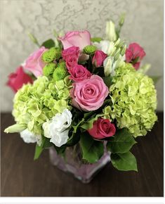 a vase filled with pink, green and white flowers on top of a wooden table