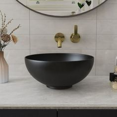 a black bowl sink sitting on top of a white counter next to a vase with flowers