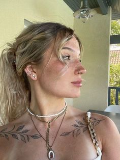 a woman with tattoos on her chest wearing a white top and silver chain around her neck