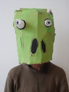 a person wearing a green paper mask with googly eyes