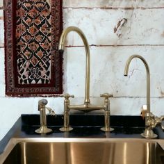 a kitchen sink with two faucets and a rug hanging on the wall