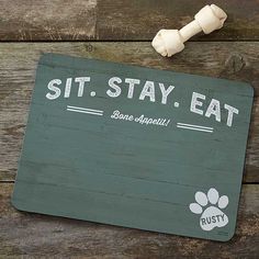 a sign that says sit stay eat with a dog paw next to it on a wooden table