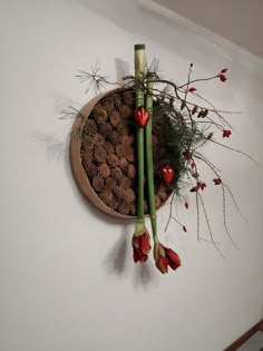 a wall mounted planter with flowers and pine cones on the top, hanging from a white wall