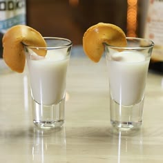 two shot glasses filled with white liquid and orange peels