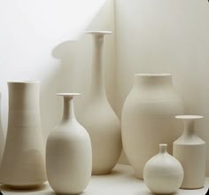 several white vases lined up against a wall