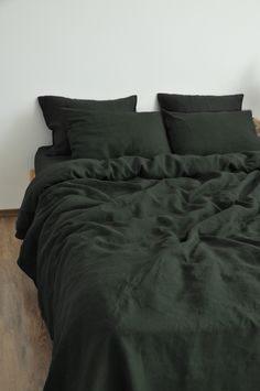 a bed with dark green sheets and pillows