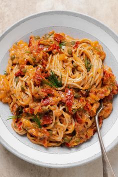 a white bowl filled with pasta covered in tomato sauce and topped with fresh herbs on top