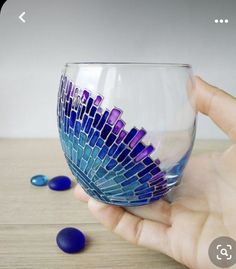 a hand holding a wine glass with purple and blue designs on the outside, sitting on top of a wooden table