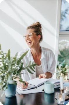 a woman sitting at a table laughing and writing