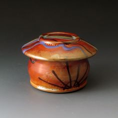 an orange and blue ceramic container sitting on top of a gray surface with lines painted on it