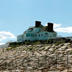 a large house sitting on top of a rocky hill next to a fenced in area