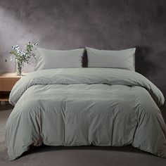 a bed with green sheets and pillows in front of a purple wall next to a table