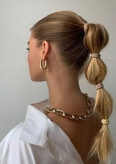 a woman with two ponytails in her hair wearing gold hoop earrings and a white blouse