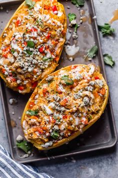 two stuffed butternuts on a baking sheet with cheese and herbs sprinkled on top