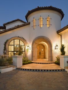 a large white house with lots of windows and plants on the front porch at night