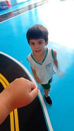 a young boy standing on top of a basketball court next to a hand holding something