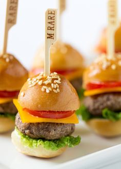 mini hamburgers with cheese, tomato and lettuce are on a white plate