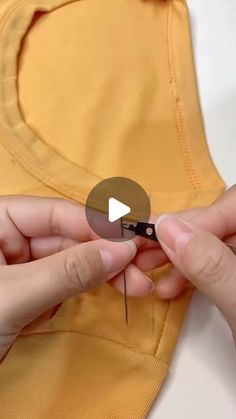 two hands are holding scissors and sewing the top of a t - shirt