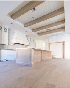 an empty kitchen with wood floors and white cabinets in the center, along with wooden beams