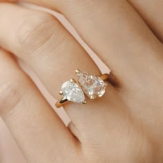 a woman's hand holding an engagement ring with two pear shaped diamonds