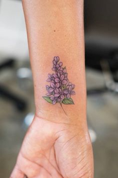 a woman's arm with a small purple flower tattoo on the left side of her wrist