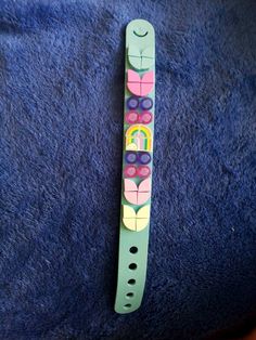 a green watch with colorful flowers on it sitting on a blue towel next to a wooden clock