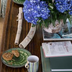 a table with blue flowers, cookies and coffee cup on it next to an open book