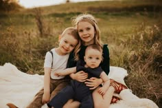 three children are sitting on a blanket in the grass and one is holding another child