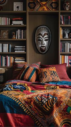 a bed with colorful blankets and pillows in front of a book shelf filled with books