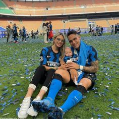 a man and woman sitting on top of a field with a baby in their arms